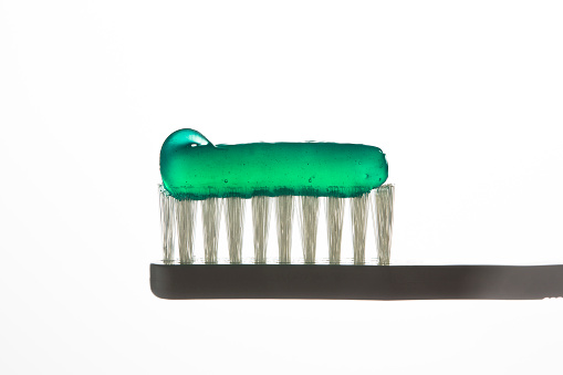 Black plastic toothbrush with green gel toothpaste. Mint or spearmint flavor. Extreme close-up of the bristle.