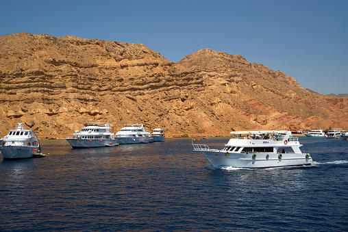 Sharm El Sheikh, Egypt - June 10, 2019: Tourist boats attraction by coastal Red Sea near Sharm El Sheikh, Egypt. Unknown people are relaxing on the deck of cruise white ships