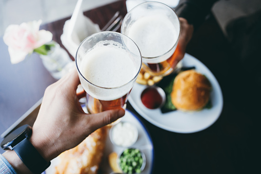 Cropped image of people toasting beers. Friends are celebrating and enjoying themselves in the restaurant.