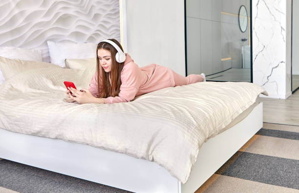 młoda kobieta 20 lat leży w łóżku na brzuchu i słucha muzyki przez słuchawki. - 18 19 years audio zdjęcia i obrazy z banku zdjęć