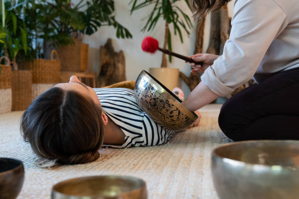 tibetische klangschalen-massage zur erholung: frau nutzt klangtherapie zur stresserholung zu hause - music wellbeing rin gong bowl stock-fotos und bilder