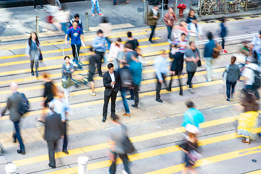 High angle view of male corporate professional in early 40s standing in middle of crosswalk on busy street checking smart phone in Hong Kong Central District.