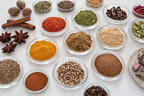 samples of different spices in glass bowls on a white background