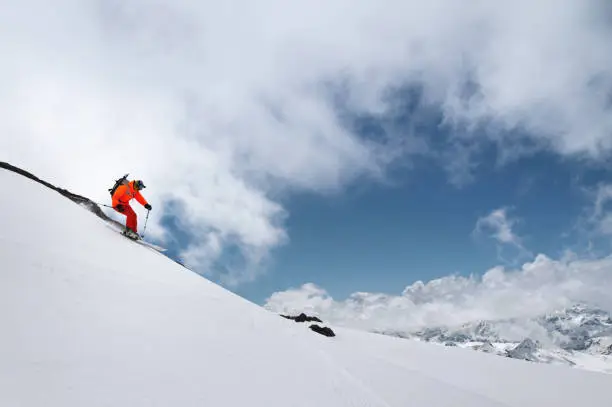 Photo of skier in bright clothes quickly descends the mountain through the snow