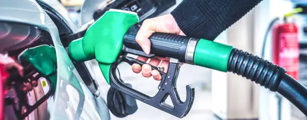 Woman pumping gasoline fuel in car at gas station.