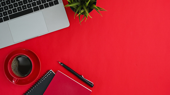 Top view of workspace with, computer laptop, house plant, notebook, coffee cup and copy space on red background.