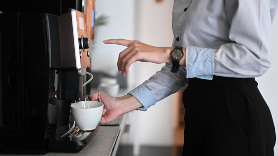 Vista de cerca de la joven haciendo café con cafetera durante el tiempo de descanso de la oficina. photo