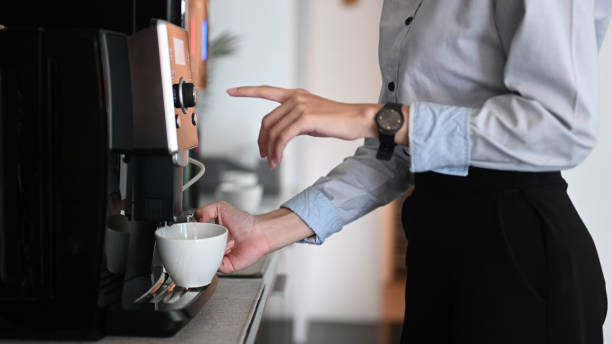 fermez-vous vers le haut de la vue de jeune femme faisant le café avec la machine à café pendant le temps de rupture de bureau. - pause café photos et images de collection