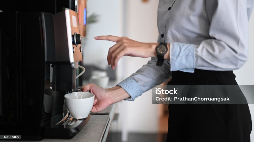 Close up view of young woman making coffee with coffee machine during office break time. Coffee - Drink Stock Photo