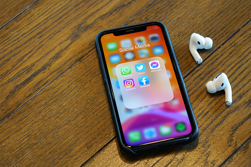 iPhone 11 Pro showing Social media applications on its screen with a pairs of AirPods Pro