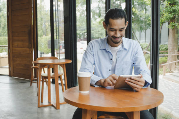 istock businessman using digital mobile tablet with hot coffee cup on desk sitting and keep distance to protect infection coronavirus (covid-19) in cafe restaurant, internet, social distancing concept 1314149577