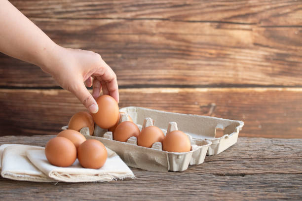 kobieta trzyma jaja kurze, brązowe jaja, organiczne jajko na perkalu w drewnianym rustykalnym stole. koncepcja produktu naturalne jaja. - animal egg eggs basket yellow zdjęcia i obrazy z banku zdjęć