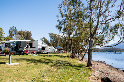 RV caravans camping at the caravan park on a peaceful lake with mountains on the horizon. Camping vacation family travel concept