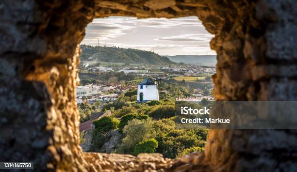 Old Windmill Through Small Window In Obidos Fortress Wall Portugal Evening Sunlight Stock Photo - Download Image Now