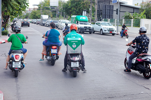 Motorcycle driving people and home delivery person  on Wanghin Road in Bangkok Ladprao. In background are queued traffic and cars on opposite side of junction