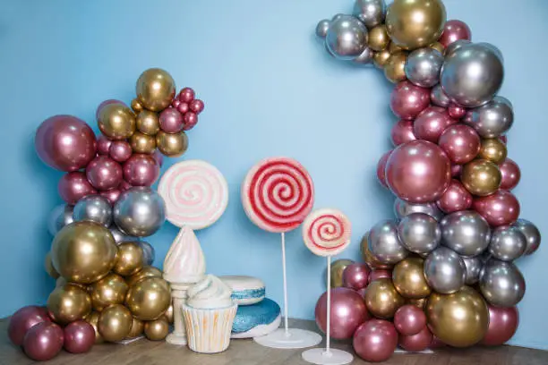 Photo of Festive decorations on a light blue background. Trees made of shiny colorful balloons, huge macaroons, ice cream and caramel on sticks