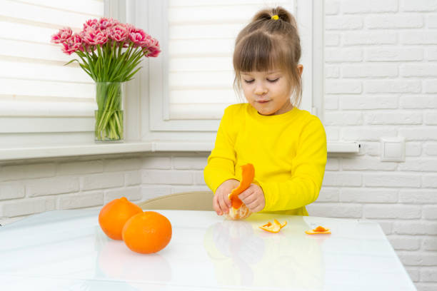 istock Girl peeling fresh tangerines at table in kitchen, closeup 1314176666