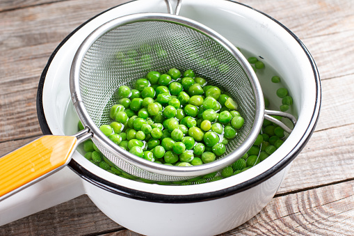 Green peas in a colander. Boiled or blanched vegetables on a wooden table