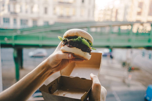istock Man holding a burger in take out box in front of the open window, coronavirus lockdown concept 1314198488