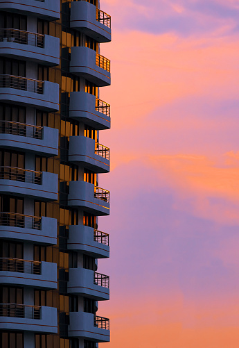 Sunlight reflection on balconies surface of high residential building with colorful sunset sky background in vertical frame