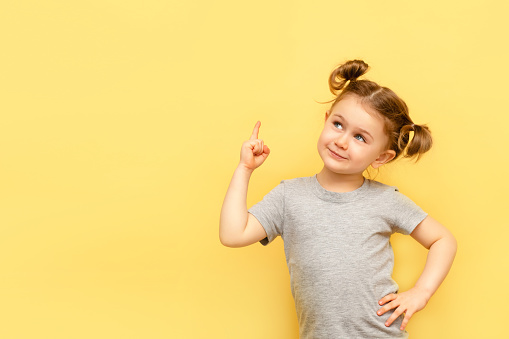 Portrait of child girl with finger pointed up. Little kid in pose has idea isolated on yellow blackboard. Success, bright idea, creative ideas and innovation technology concept
