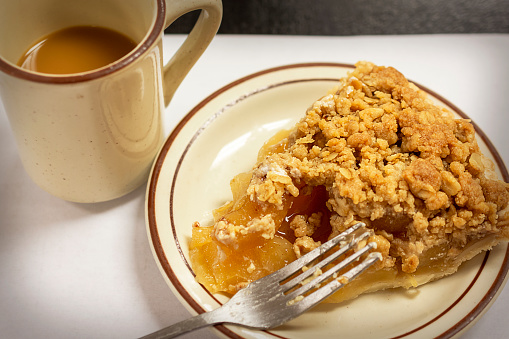 Dutch Apple Pie, Apple Crumble Pie, or Apple Streusel Pie and a cup of coffee on a diner counter with a blank paper placemat.