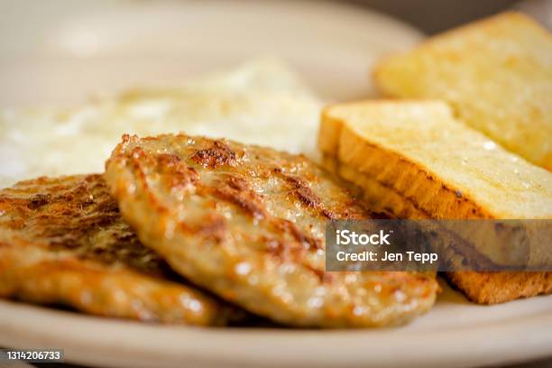 A Dish At A Breakfast Diner Including 2 Pork Sausage Patties Two Pieces Of White Toast And 2 Over Easy Eggs Blurred In The Background Stock Photo - Download Image Now