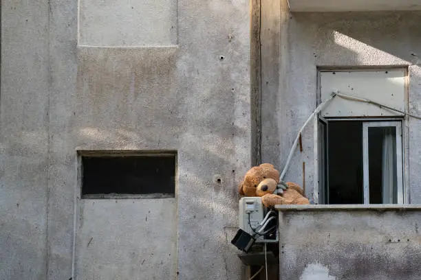 A teddy bear left in a balcony of an old neglected building.