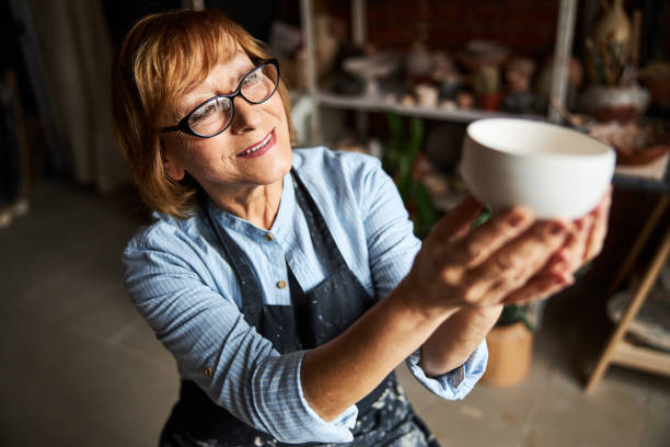 istock Charming female potter looking at clay bowl in pottery workshop 1314210146