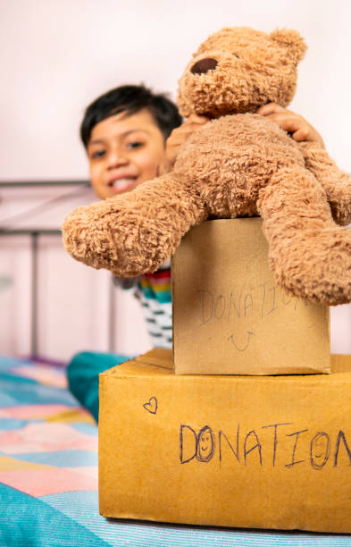 Happy little boy sitting on the bed in a packed donation box.