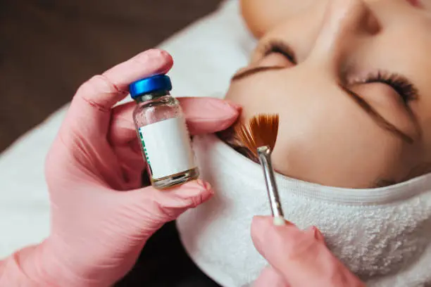 Photo of in the hands of a brush and a container with the drug, cosmetology chemical peeling