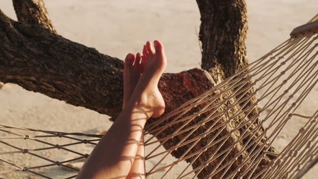close up feet of asian woman resting and sleeping on hammock at beach in summer vacation