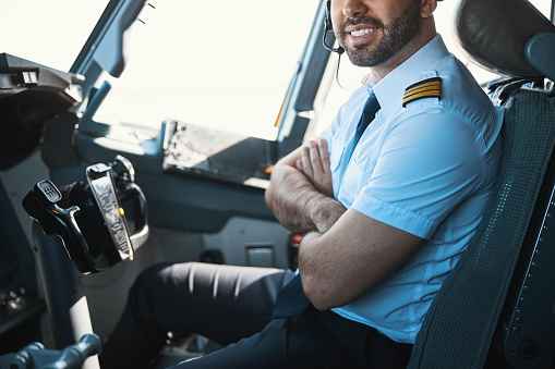 Cropped photo of a smiling Caucasian pilot sitting in the cockpit with his arms crossed