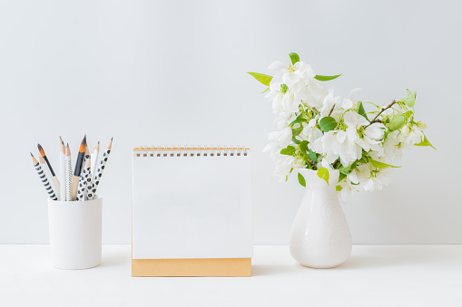Mockup white desk calendar and with spring flowers in a vase on a light background