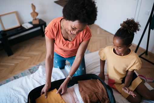 High angle view of a happy middle aged African American woman and her young daughter at home, packing their bags for a vacation, smiling