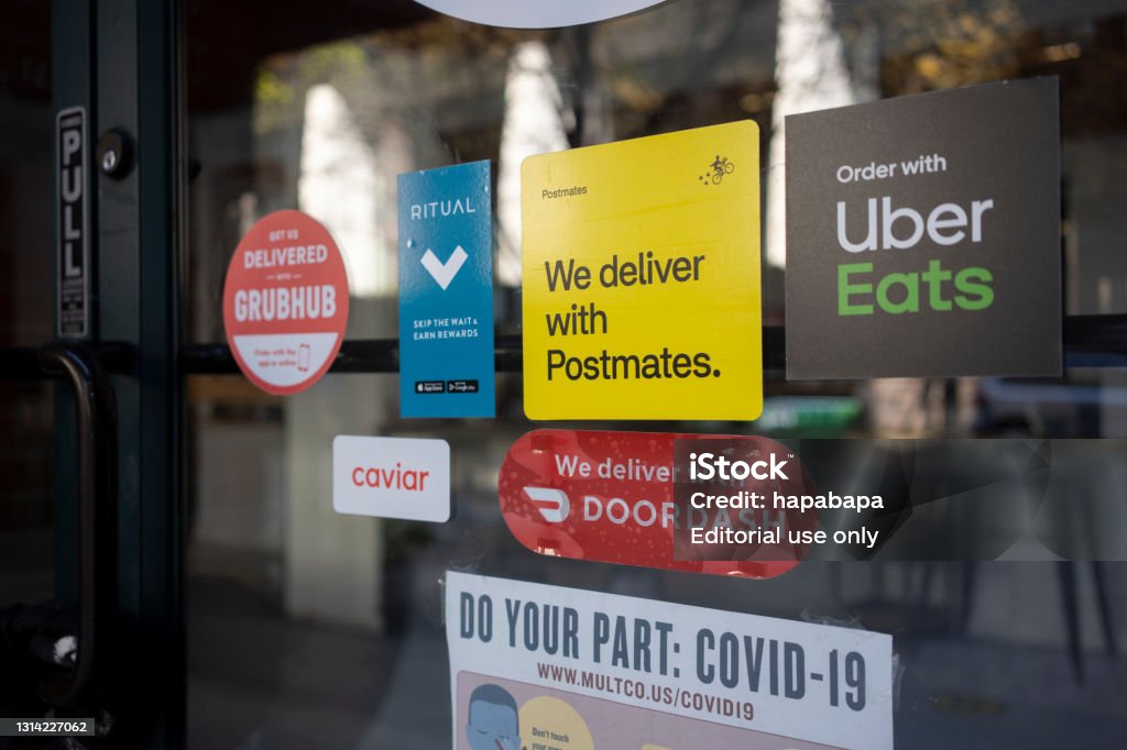 Food Delivery Services Amid the Pandemic Portland, OR, USA - Apr 18, 2021: Various food delivery service options - DoorDash, Postmates, Uber Eats, Ritual, Caviar, and Grubhub - are seen advertised at the entrance to a restaurant in Portland, Oregon, during the coronavirus pandemic. DoorDash Stock Photo