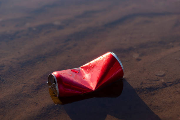Red empty dented aluminum soda can in shallow water