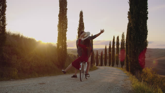 SLO MO Couple riding a retro looking bicycle on a road lined with cypresses in Tuscany