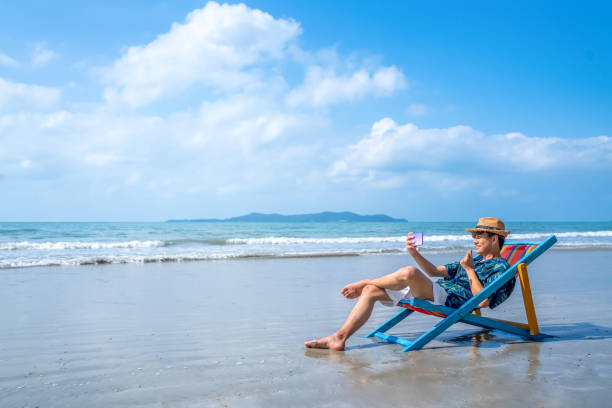 istock Young Asian man resting on beach chair with using smartphone 1314251817