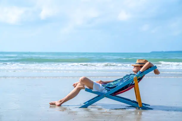 Photo of Asian man resting on beach chair on the beach at summer sunny day.