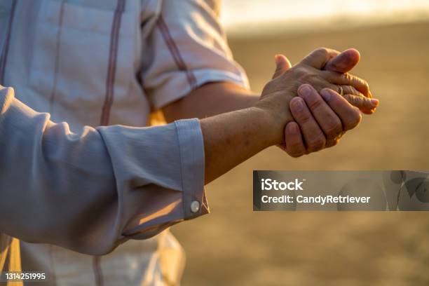 Close Up Senior Couple Husband And Wife Holding Hands Together On The Beach At Summer Sunset Stock Photo - Download Image Now