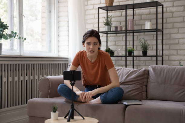 Inspired young woman sit on sofa talk before cellphone webcam