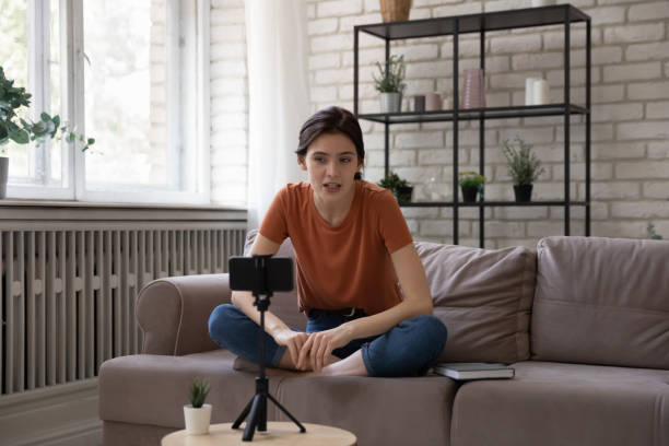 вдохновленный молодая женщина сидеть на диване говорить перед веб-камера мобильного телефона - gen z стоковые фото и изображения