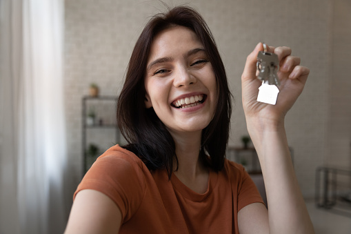 Starting new life. Overjoyed young female hold keys from new home look at camera shoot selfie portrait to share news at social network. Excited millennial lady proud of becoming homeowner first time