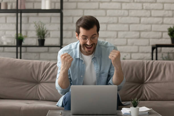 istock Euphoric young man sit by laptop shout super raise fists 1314253013