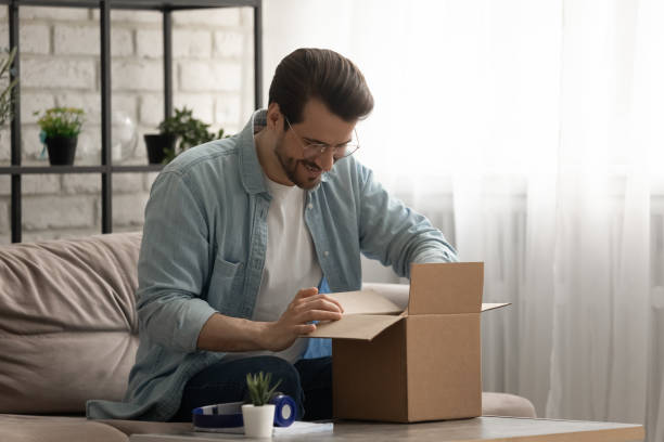istock Smiling young guy opening package with consumer goods with pleasure 1314253036