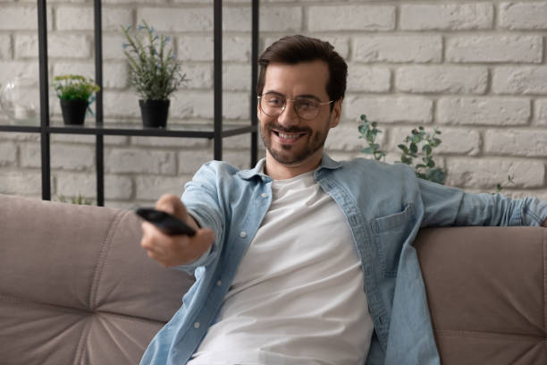 istock Millennial guy watch television at home hold tv remote control 1314253041