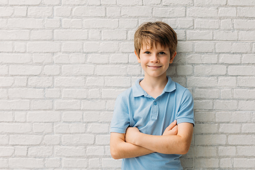 Portrait of happy young caucasian boy in casual outfit with arms crossed isolated over white bricks background smiling and looking at camera