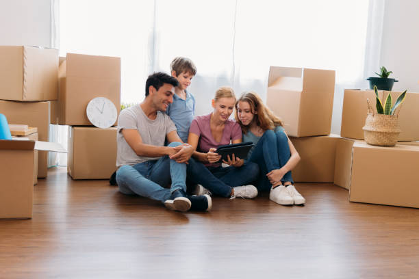 Family watching furniture in digital tablet Cheerful and beautiful caucasian mother holding digital tablet and shopping for furniture for new home with handsome husband and children with cardboard boxes around teenager couple child blond hair stock pictures, royalty-free photos & images