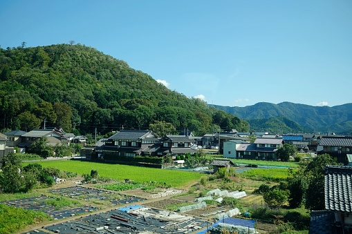 A vew of fields, houses and green hills as seen from the window of a train from Narita Airport to Tokyo.